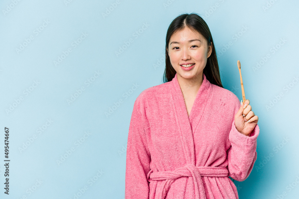 Young asian woman wearing a bathrobe brushing teeth isolated on pink background smiling and raising thumb up Young asian woman wearing a bathrobe brushing teeth isolated on pink background smiling and raising thumb up