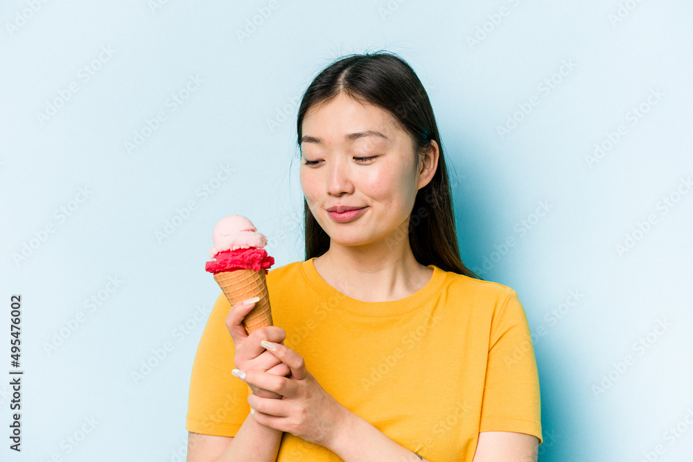 Young asian woman eating an ice cream isolated on blue background Young asian woman eating an ice cream isolated on blue background