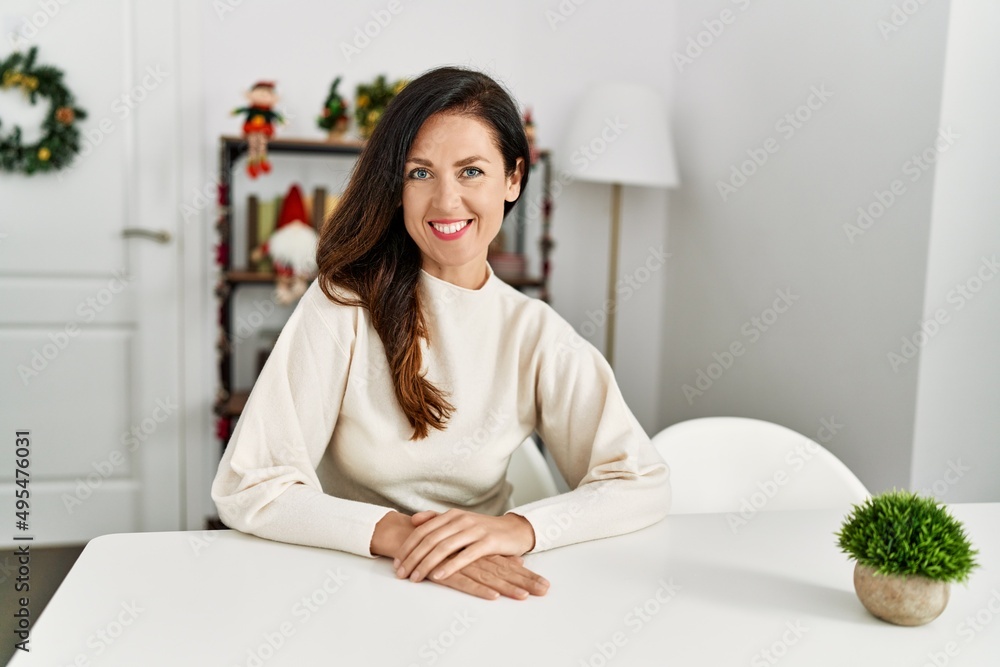 Middle age hispanic woman smiling confident sitting on the table by christmas decor at home Middle age hispanic woman smiling confident sitting on the table by christmas decor at home