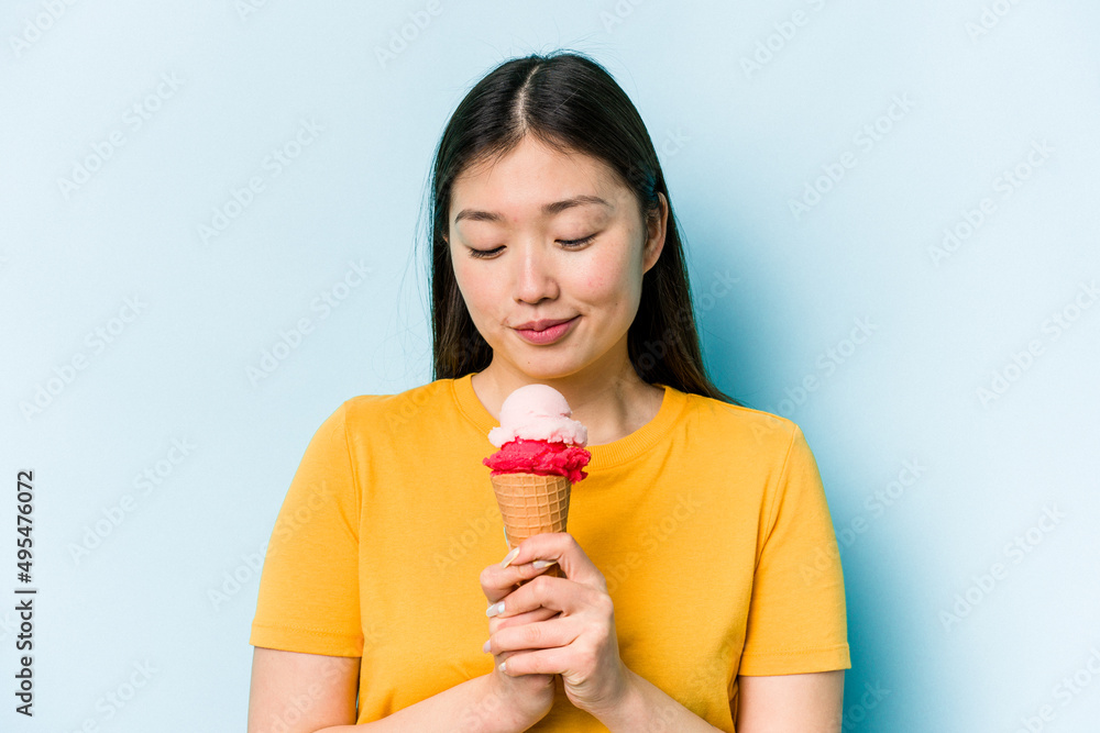 Young asian woman eating an ice cream isolated on blue background Young asian woman eating an ice cream isolated on blue background