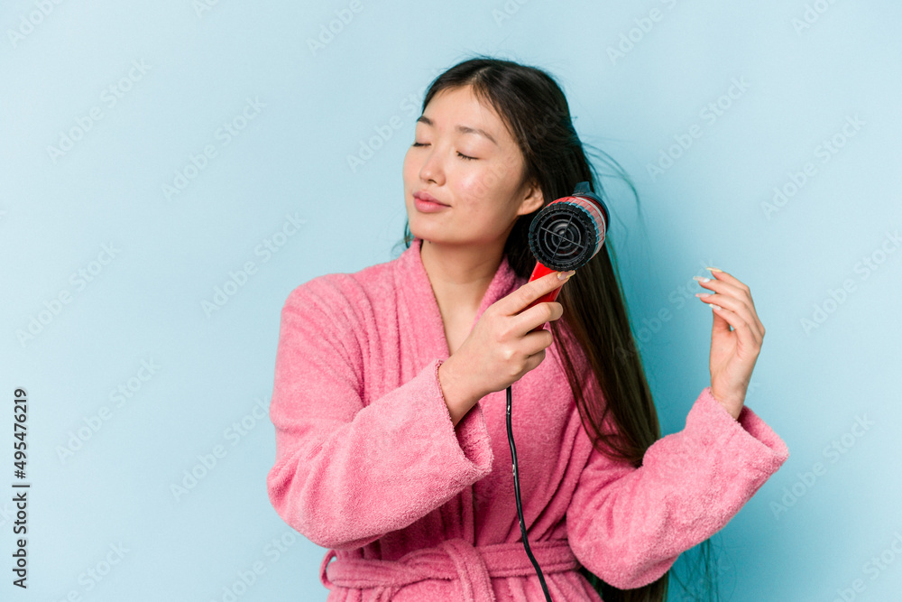Young asian woman drying hair isolated on blue background Young asian woman drying hair isolated on blue background