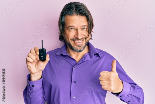 Middle age handsome man holding key of new car smiling happy and positive, thumb up doing excellent and approval sign