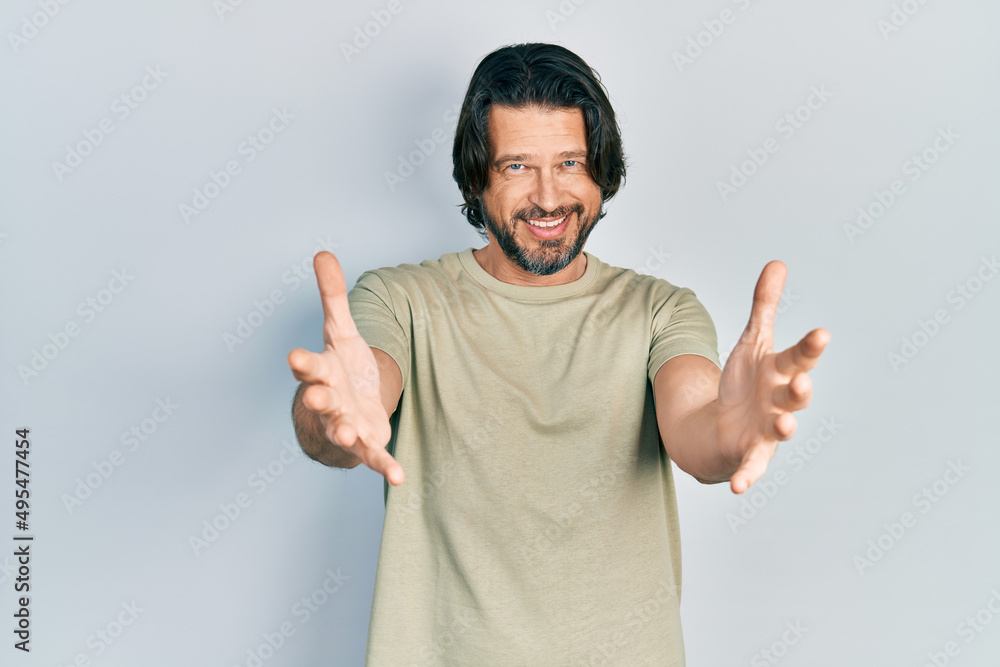 Fototapeta premium Middle age caucasian man wearing casual clothes looking at the camera smiling with open arms for hug. cheerful expression embracing happiness.