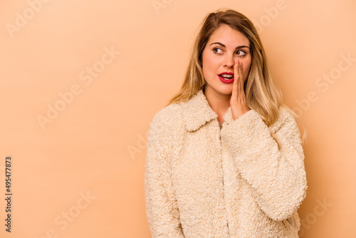 Young caucasian woman isolated on beige background is saying a secret hot braking news and looking aside © Asier