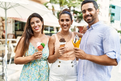 Three hispanic friends smiling happy eating ice cream at the city.