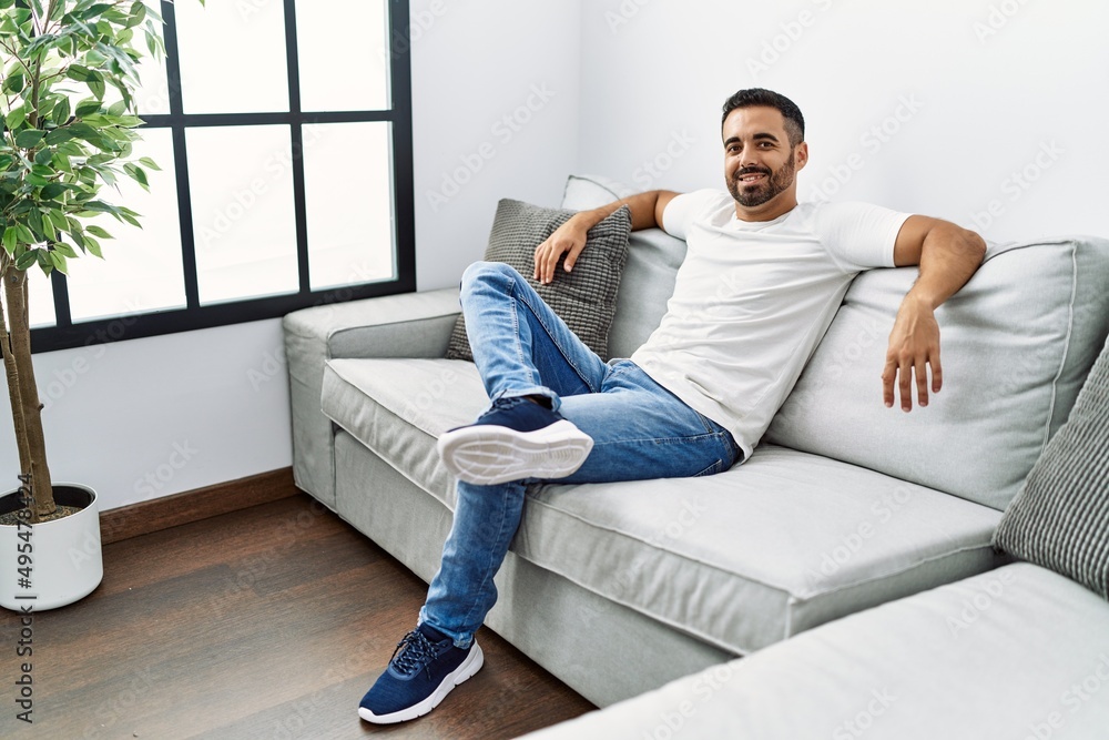 Young hispanic man smiling confident sitting on sofa at home