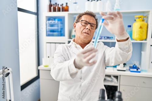 Middle age man wearing scientist uniform looking test tube at laboratory