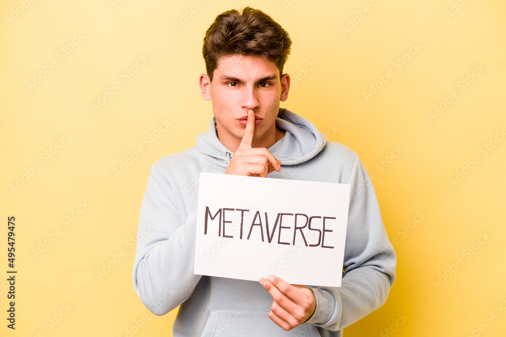 Young caucasian man holding metaverse placard isolated on yellow background keeping a secret or asking for silence. Young caucasian man holding metaverse placard isolated on yellow background keeping a secret or asking for silence.