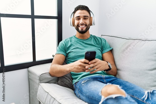 Young arab man listening to music sitting on sofa at home