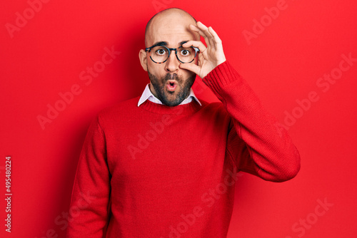 Young bald man wearing casual clothes and glasses doing ok gesture shocked with surprised face, eye looking through fingers. unbelieving expression.
