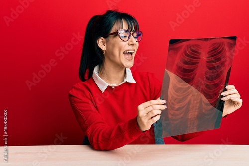 Young brunette woman with bangs holding chest radiography smiling and laughing hard out loud because funny crazy joke.