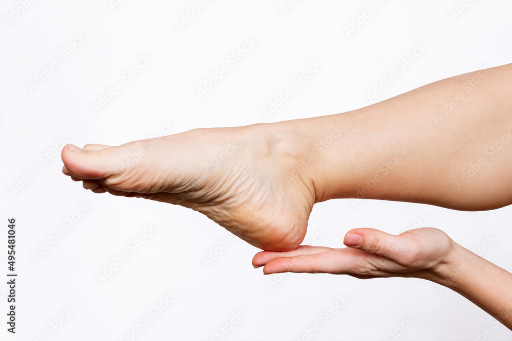 Cropped shot of a young woman touching the dry heel with her hand. The girl moisturizing the cracked foot with a cream for skin softness isolated on a white background. Skin care concept