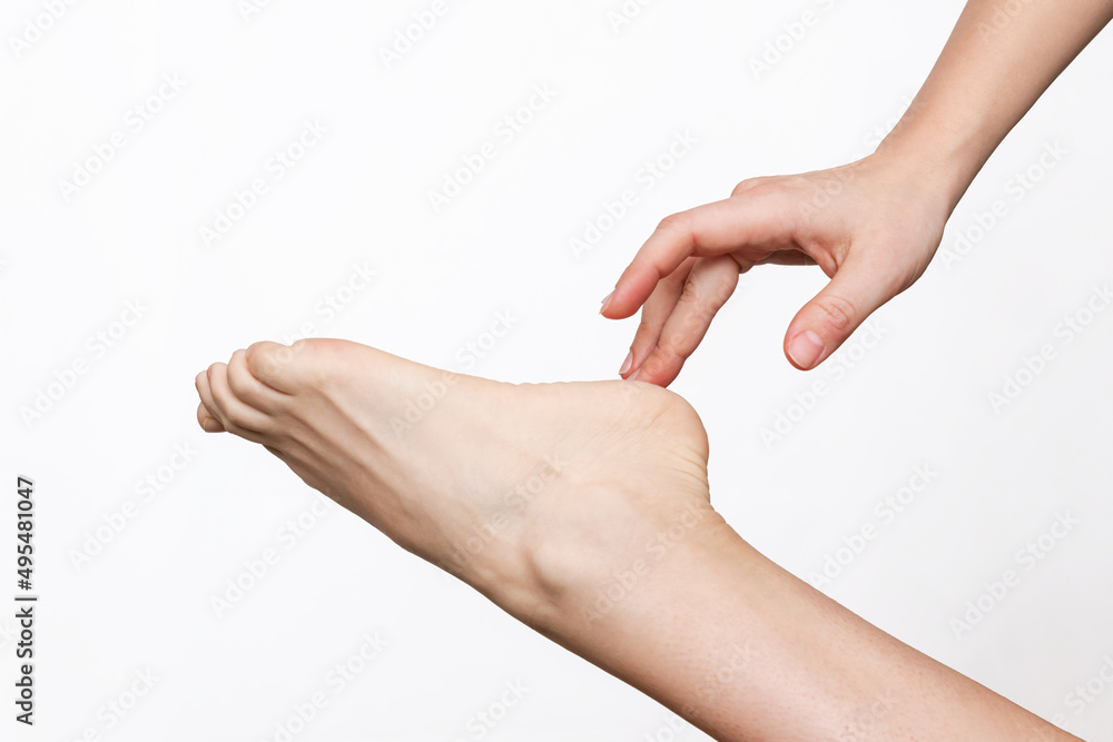 Cropped shot of a young woman touching the heel with her fingers. The girl moisturizing the dry cracked foot with a cream for skin softness isolated on a white background. Skin care concept