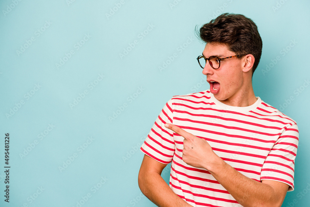 Young caucasian man isolated on blue background points with thumb finger away, laughing and carefree. Young caucasian man isolated on blue background points with thumb finger away, laughing and carefree.