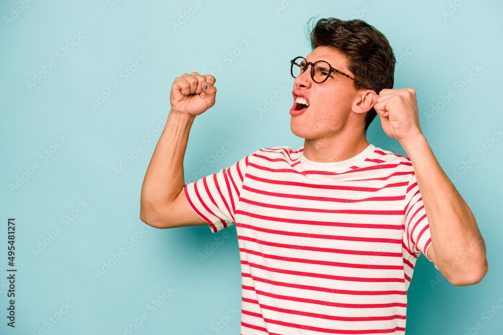 Young caucasian man isolated on blue background raising fist after a victory, winner concept. Young caucasian man isolated on blue background raising fist after a victory, winner concept.