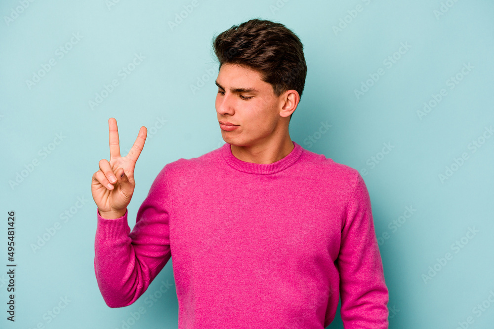 Young caucasian man isolated on blue background joyful and carefree showing a peace symbol with fingers. Young caucasian man isolated on blue background joyful and carefree showing a peace symbol with fingers.