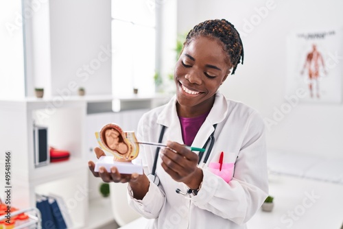 African american woman wearing doctor uniform holding anatomical model of uterus with fetus at clinic photo