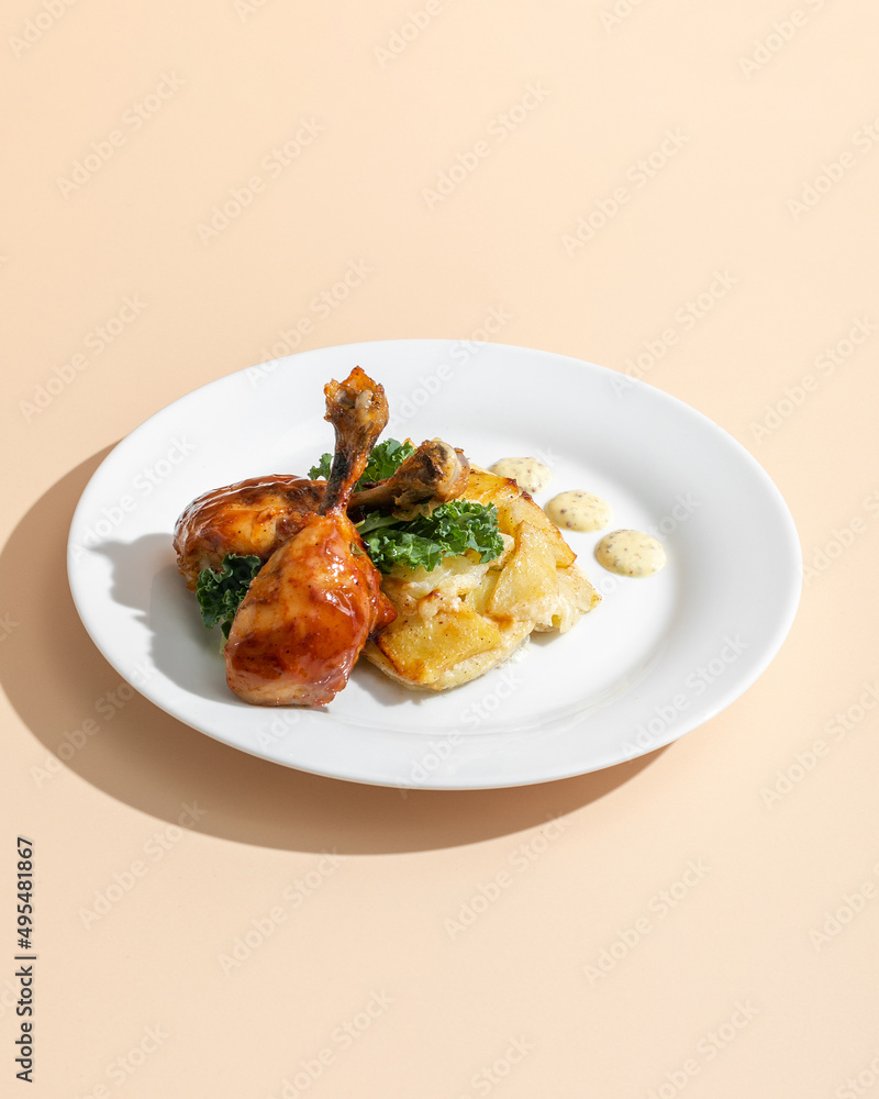 Duck legs confit with gratin on white plate on beige background Duck legs confit with gratin on white plate on beige background