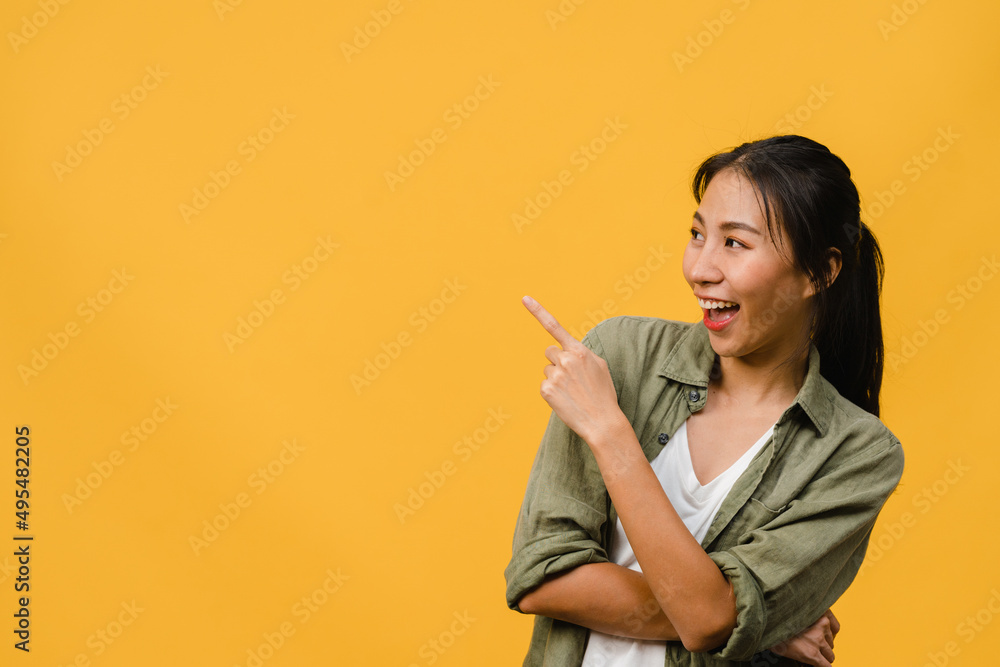 Portrait of young Asian lady smiling with cheerful expression, shows something amazing at blank space in casual clothing and standing isolated over yellow background. Facial expression concept. Portrait of young Asian lady smiling with cheerful expression, shows something amazing at blank space in casual clothing and standing isolated over yellow background. Facial expression concept.