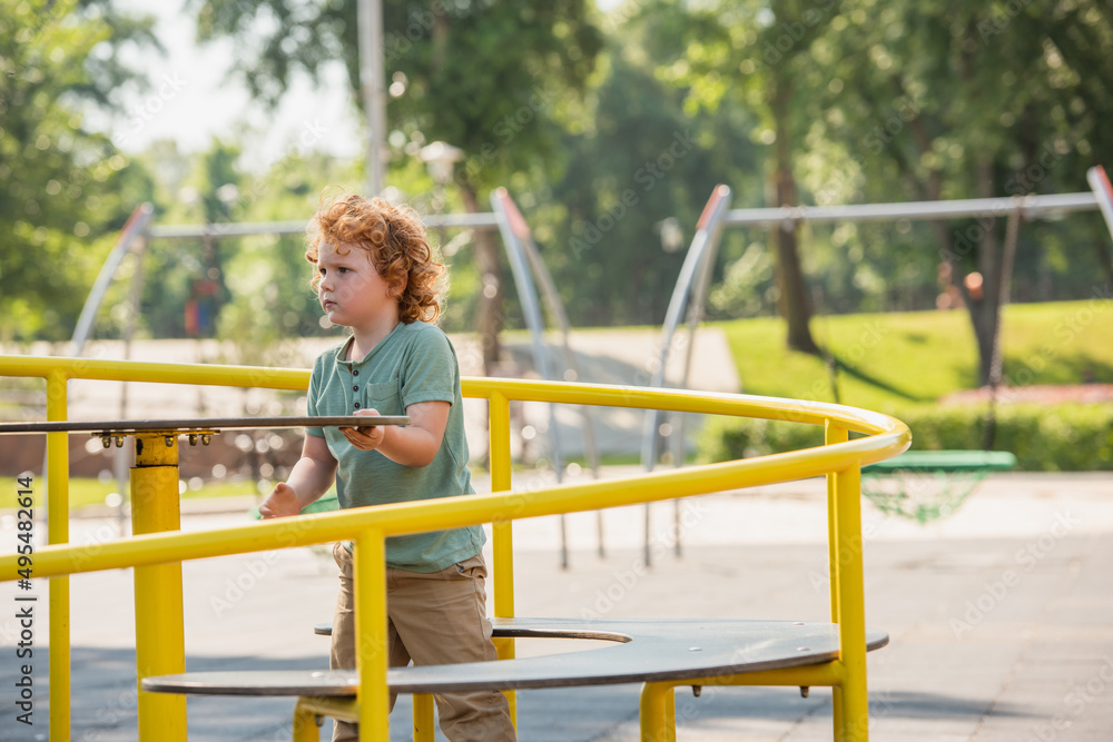 curly boy having fun on carousel in summer park. curly boy having fun on carousel in summer park.