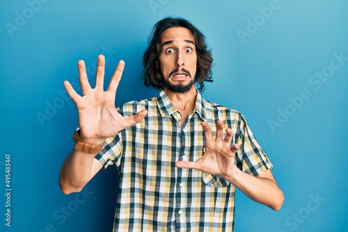 Young hispanic man wearing casual clothes afraid and terrified with fear expression stop gesture with hands, shouting in shock. panic concept.