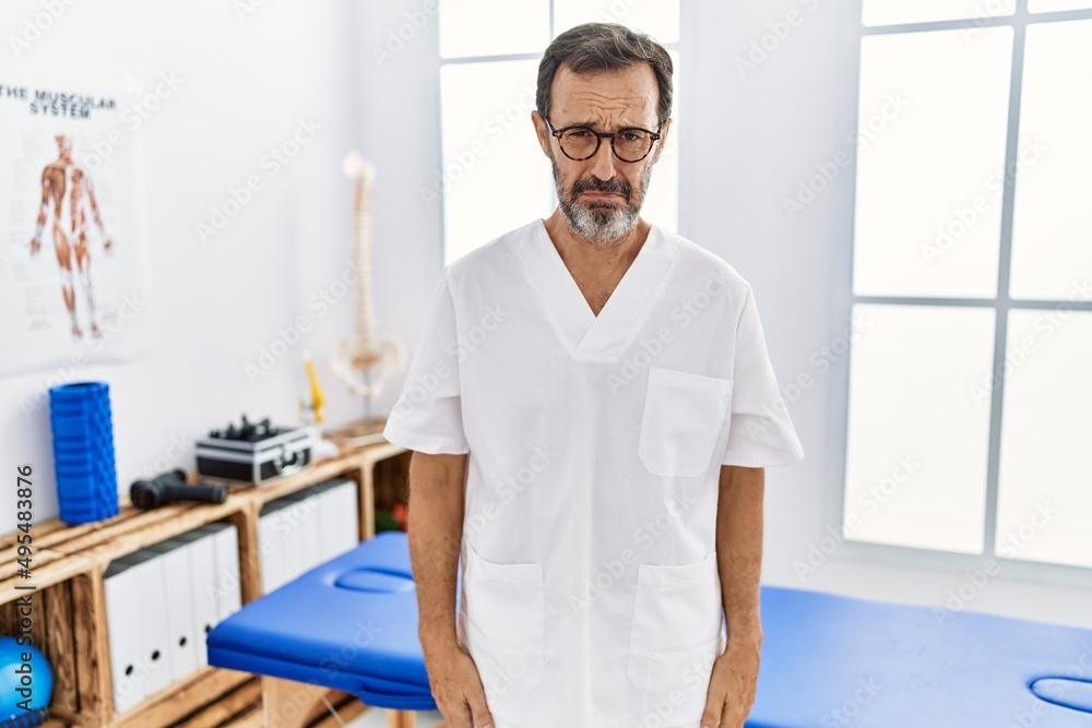 Middle age man with beard working at pain recovery clinic depressed and worry for distress, crying angry and afraid. sad expression.