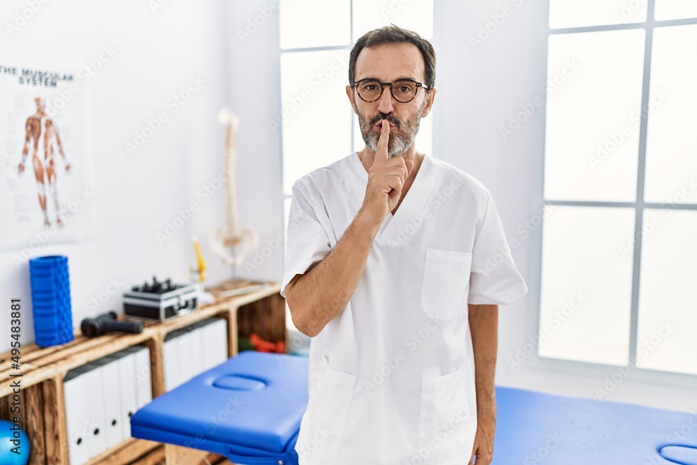 Middle age man with beard working at pain recovery clinic asking to be quiet with finger on lips. silence and secret concept. Middle age man with beard working at pain recovery clinic asking to be quiet with finger on lips. silence and secret concept.