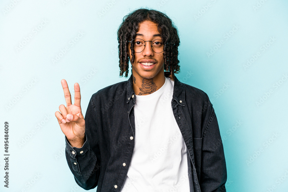 Young African American man isolated on blue background showing victory sign and smiling broadly. Young African American man isolated on blue background showing victory sign and smiling broadly.