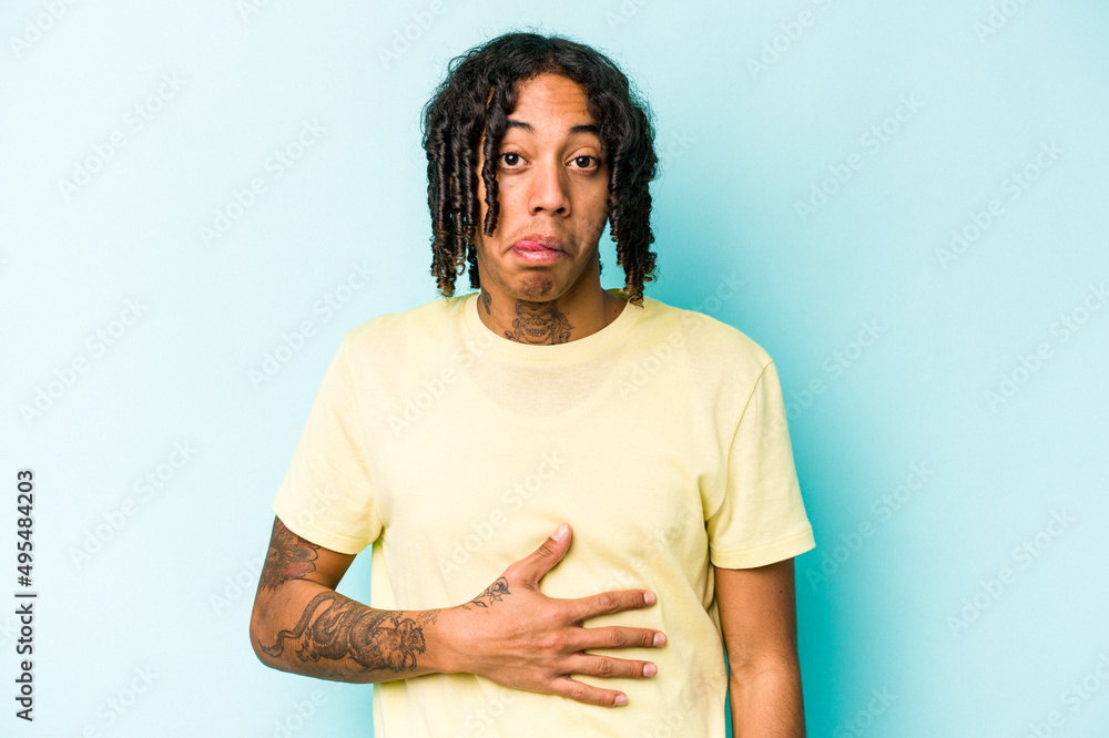 Young African American man isolated on blue background touches tummy, smiles gently, eating and satisfaction concept. Young African American man isolated on blue background touches tummy, smiles gently, eating and satisfaction concept.