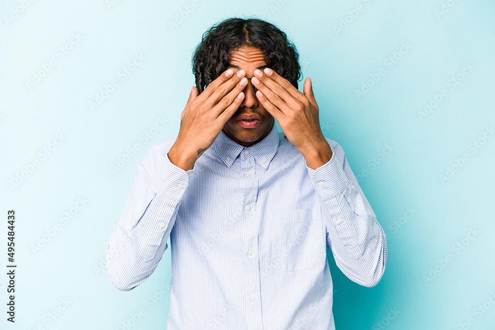 Young African American man isolated on blue background afraid covering eyes with hands. Young African American man isolated on blue background afraid covering eyes with hands.