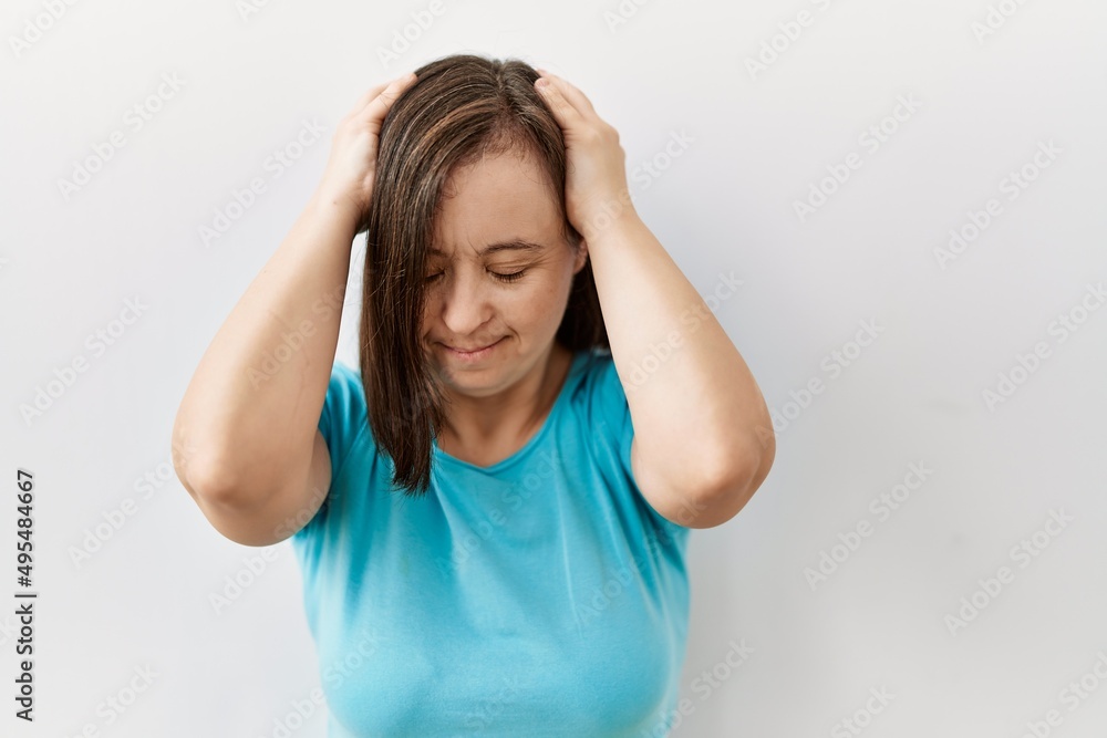 Young down syndrome woman standing over isolated background suffering from headache desperate and stressed because pain and migraine. hands on head. Young down syndrome woman standing over isolated background suffering from headache desperate and stressed because pain and migraine. hands on head.