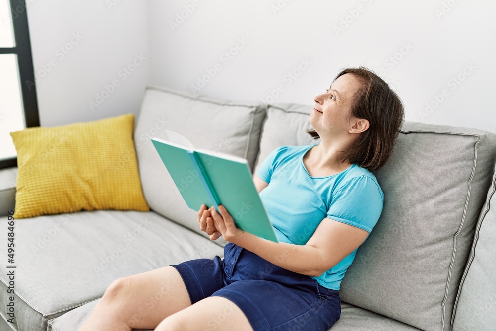 Brunette woman with down syndrome sitting on the sofa reading a book at the living room Brunette woman with down syndrome sitting on the sofa reading a book at the living room