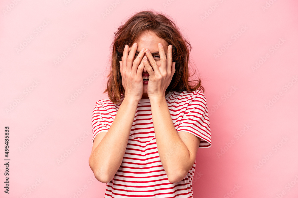 Young caucasian woman isolated on pink background blink at the camera through fingers, embarrassed covering face. Young caucasian woman isolated on pink background blink at the camera through fingers, embarrassed covering face.