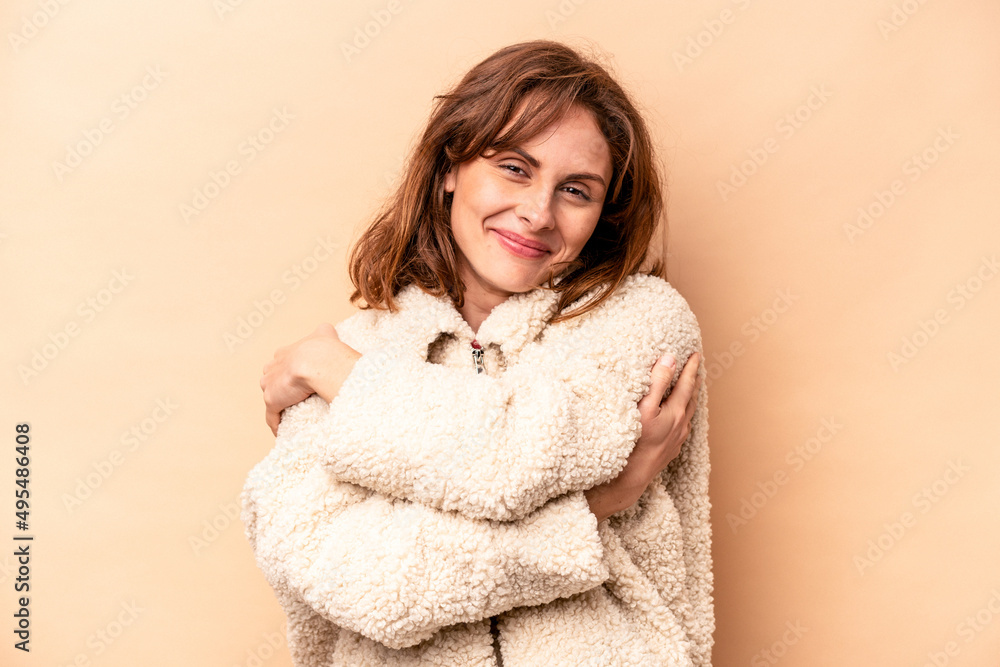 Young caucasian woman isolated on beige background hugs, smiling carefree and happy. Young caucasian woman isolated on beige background hugs, smiling carefree and happy.