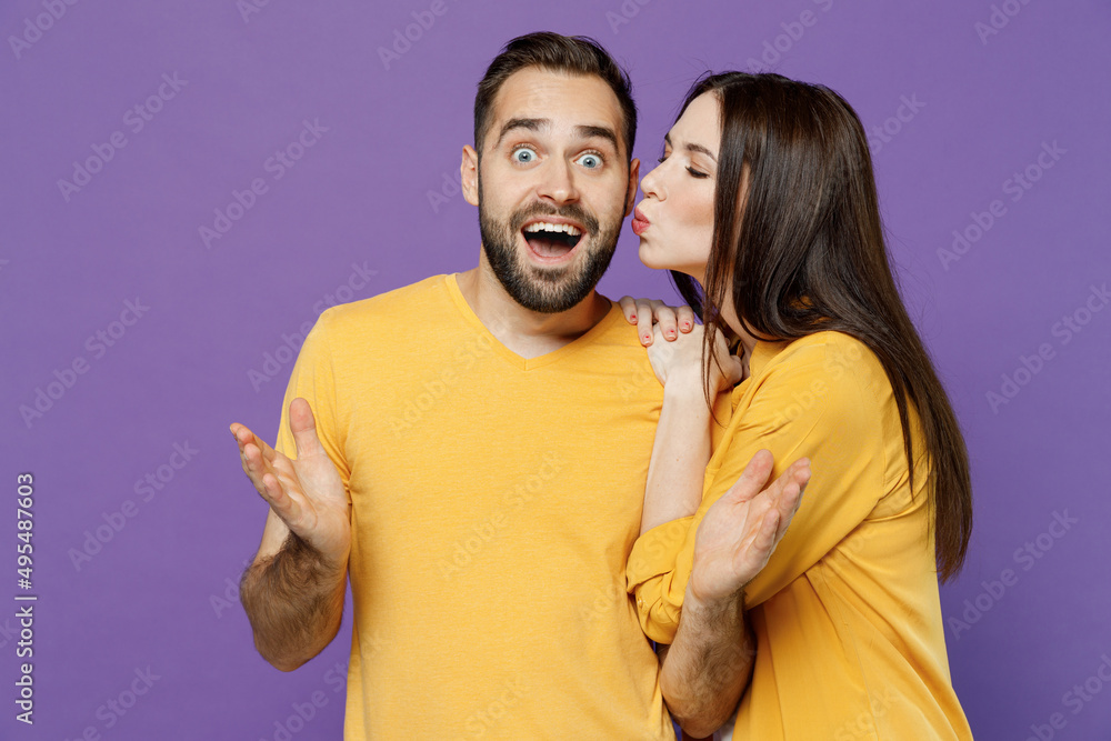 Young excited happy fun couple two friends family man woman 20s together wearing yellow casual clothes looking camera kiss cheek spread hands isolated on plain violet color background studio portrait. Young excited happy fun couple two friends family man woman 20s together wearing yellow casual clothes looking camera kiss cheek spread hands isolated on plain violet color background studio portrait.