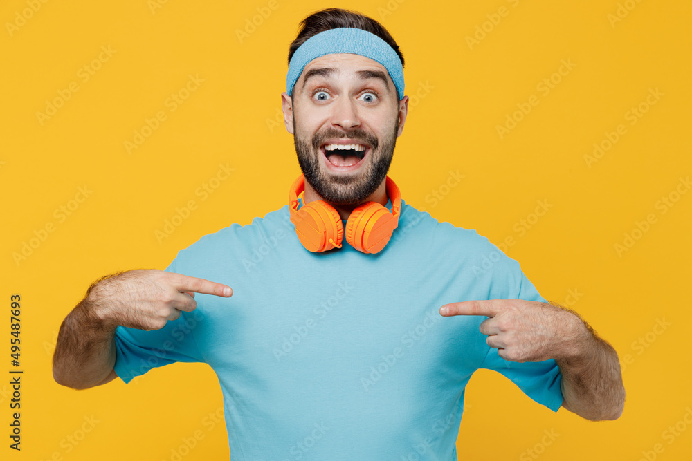 Young fitness trainer instructor sporty man sportsman in headband blue t-shirt spend weekend in home gym point fingers on himself isolated on plain yellow background. Workout sport lifestyle concept. Young fitness trainer instructor sporty man sportsman in headband blue t-shirt spend weekend in home gym point fingers on himself isolated on plain yellow background. Workout sport lifestyle concept.