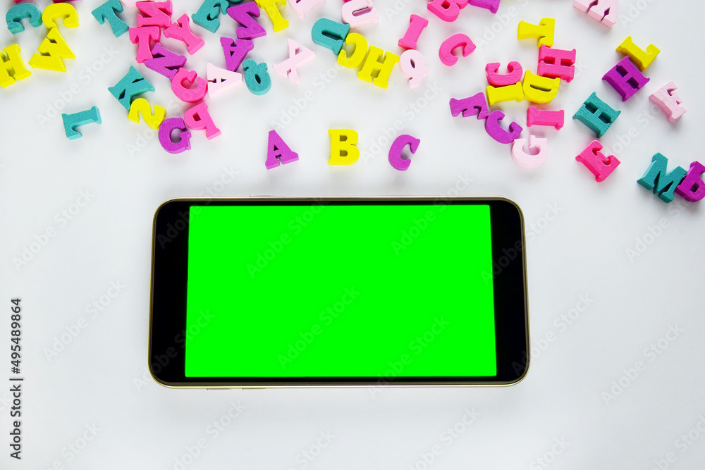 Close-up of a foreign alphabet and a mobile phone with a blank green screen lie on a light background, top view. English course online. Moskap for advertising Close-up of a foreign alphabet and a mobile phone with a blank green screen lie on a light background, top view. English course online. Moskap for advertising