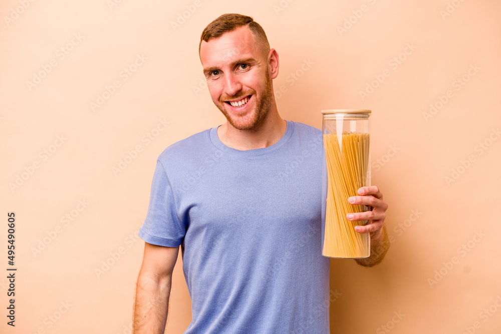 Young caucasian man holding spaghettis jar isolated on beige background happy, smiling and cheerful. Young caucasian man holding spaghettis jar isolated on beige background happy, smiling and cheerful.