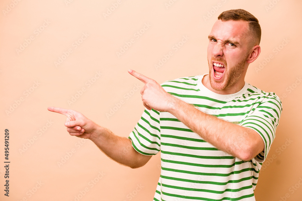 Young caucasian man isolated on beige background pointing with forefingers to a copy space, expressing excitement and desire. Young caucasian man isolated on beige background pointing with forefingers to a copy space, expressing excitement and desire.