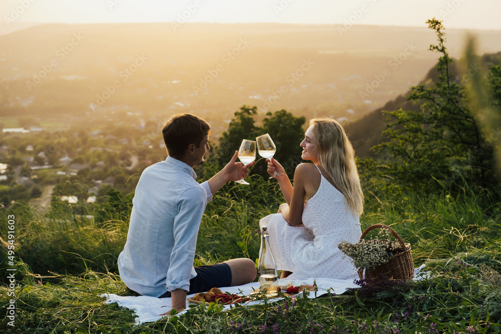 Romantic couple having happy on summer picnic, sitting on the hill, eating and drinking wine.
