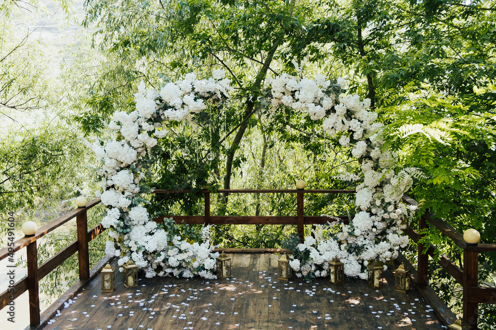 Round wedding arch decorated with white flowers and greenery in the park. Outdoor Wedding Ceremony.