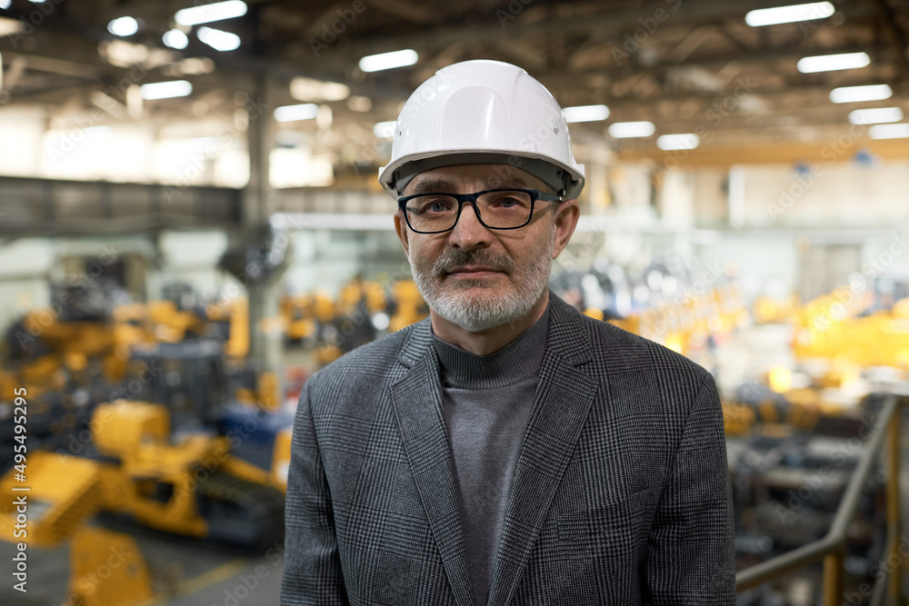 Portrait of elder engineer in hardhat looking at camera while running the process in plant Portrait of elder engineer in hardhat looking at camera while running the process in plant