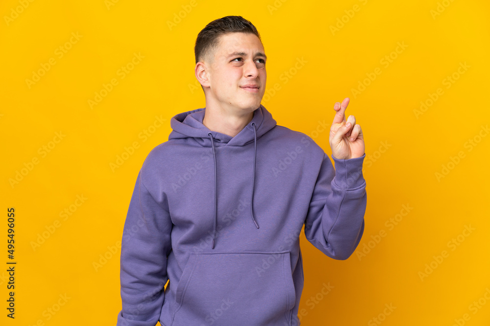 Young caucasian man isolated on yellow background with fingers crossing and wishing the best Young caucasian man isolated on yellow background with fingers crossing and wishing the best