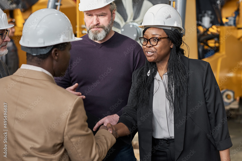 Business partners in work helmets greeting each other and shaking hands during meeting in plant Business partners in work helmets greeting each other and shaking hands during meeting in plant