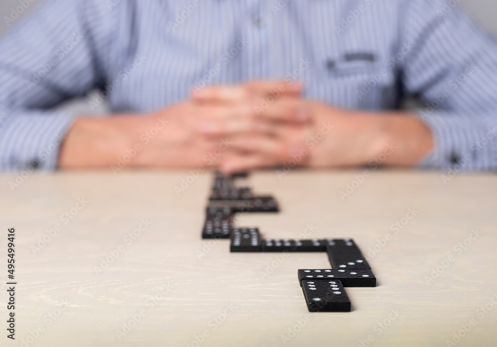 Businessman sitting at table with domino and thinking of action plan. Strategy, risk assessment concept. High quality photo Businessman sitting at table with domino and thinking of action plan. Strategy, risk assessment concept. High quality photo