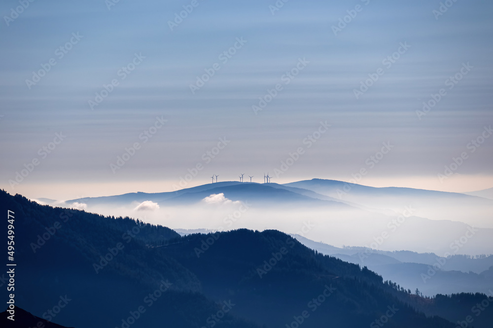 Panoramic view on wind turbines in the Hochschwab Region in Upper Styria, Austria. Cloudless weather on sunny summer day in the Alps. Blue misty valley and soft hills. Concept green energy. Wind mill