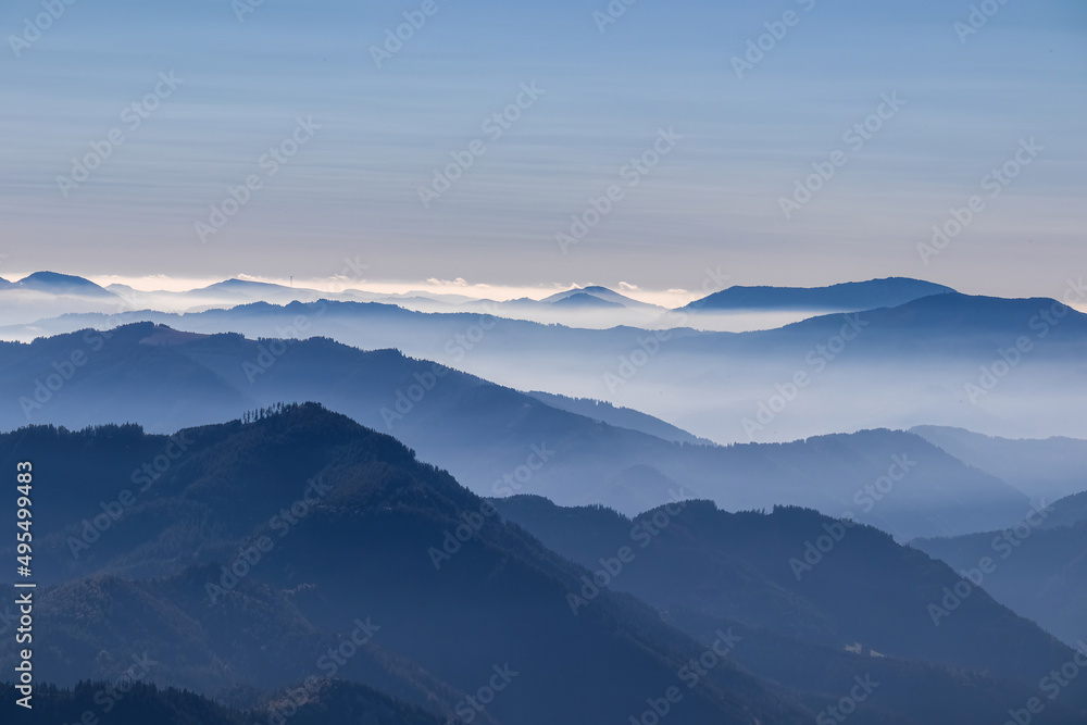 A panoramic view on the mountain peaks of the Hochschwab Region in Upper Styria, Austria. Cloudless weather on a sunny summer day in the Alps. Blue misty valley and soft hills. Concept freedom