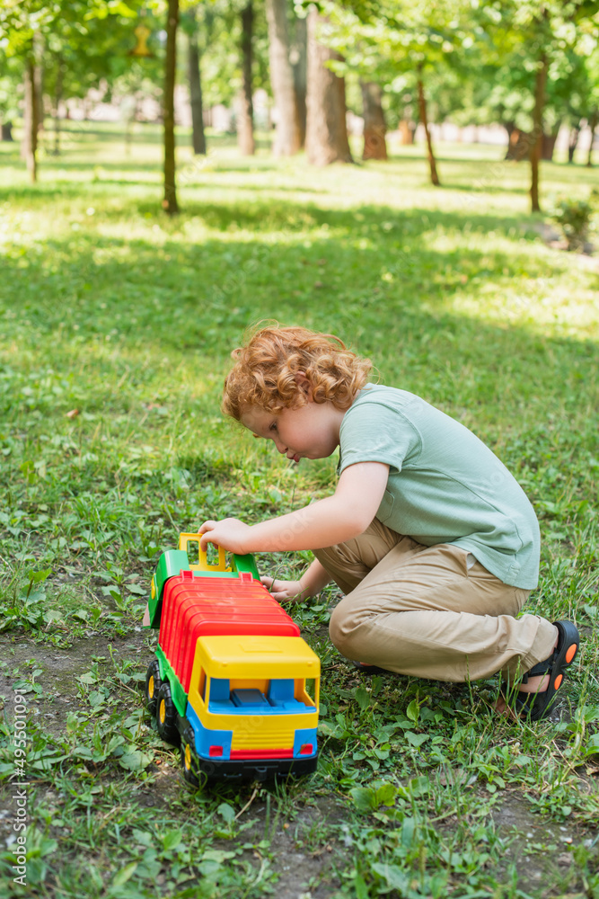 full length view of boy playing with toy truck on green grass. full length view of boy playing with toy truck on green grass.