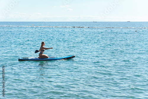 Young female surfer in bikini riding standup paddleboard in ocean.