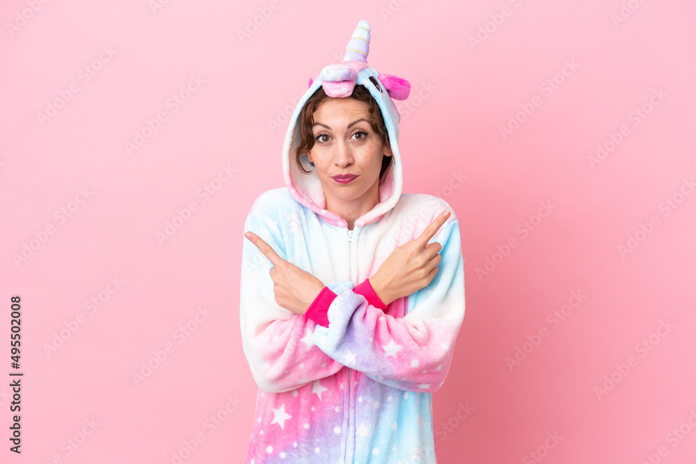 Young caucasian woman with unicorn pajamas isolated on pink background pointing to the laterals having doubts Young caucasian woman with unicorn pajamas isolated on pink background pointing to the laterals having doubts